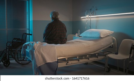 Depressed senior man sitting on the hospital bed alone at night, he feels lonely and abandoned - Powered by Shutterstock