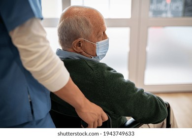 Depressed senior patient sitting on wheelchair and wearing protective face mask during covid-19 pandemic. Nurse assisting sad elderly man using wheelchair wearing surgical face mask. - Powered by Shutterstock