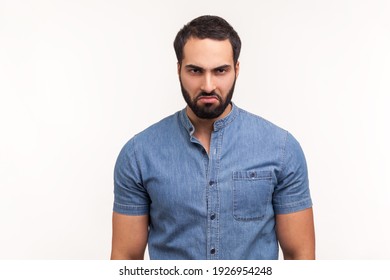 Depressed sorrowful bearded man in blue shirt looking at camera with unhappy sad expression, tired of being lonely. Indoor studio shot isolated on white background