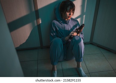 Depressed suicidal woman sitting on the floor in the dark, holding a gun and crying, thinking about committing suicide; scared woman victim of domestic violence holding a gun for self-defense
