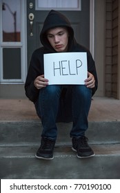 A Depressed Teen Boy Holding A Help Sign While On The Front Steps Of A House.