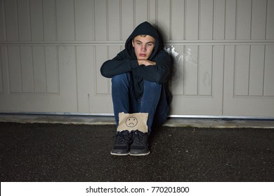 A Depressed Teen Boy Holding A Sad Face Sign In Front Of A Garage Door.