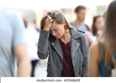 Depressed teen feeling lonely walking on the street surrounded by people