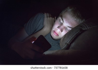 Depressed Teenage Boy Laying Down On A Couch With His Smart Phone. 