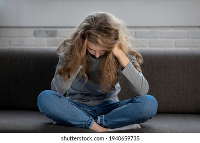 Depressed teenager girl with sad emotions and feelings sitting on the couch at home - Shutterstock ID 1940659735