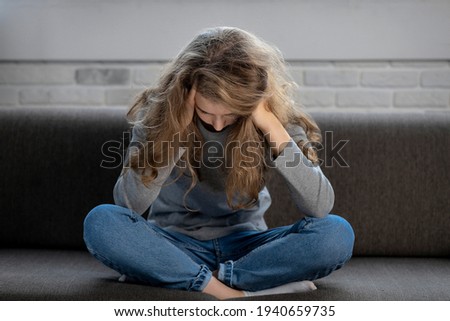 Depressed teenager girl with sad emotions and feelings sitting on the couch at home