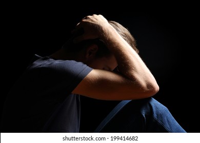 Depressed teenager man with hands over head isolated in a black background      