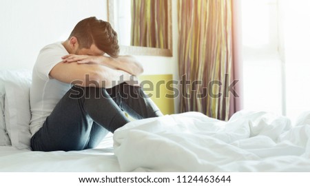Depressed or tired man sitting on bed in hotel room
