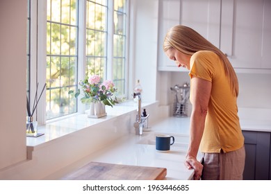 Depressed And Unhappy Mature Woman At Home Standing By Kitchen Window