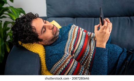 Depressed Unhappy Sad Man Using Smartphone Device While Sitting On Sofa At Home. Mature Man Lying On Couch Reading Messages On Mobile Phone. Caucasian Spanish Feeling Lonely At Home.