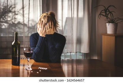 Depressed Woman Is Drinking Red Wine And Taking Pills At Home Alone. Head In Hands. Alcohol And Drug Addiction Concept. Social Issues