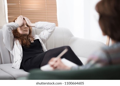 Depressed woman holding her head while sitting on a couch in a psychiatrist office