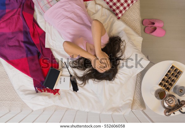 Depressed woman\
lying in bed, covering her\
face