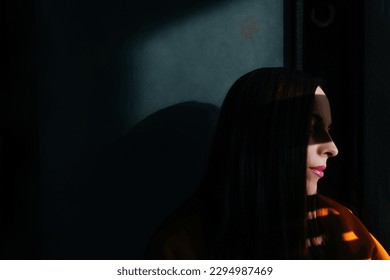Depressed woman with pink lips in dark. Sun light on half face.