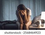 Depressed woman sitting on the bed at night, she is sad and suffering from insomnia