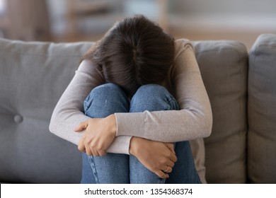 Depressed Woman Sitting On Couch Hide Head Hugging With Hands Laps And Crying Having Broken Heart Break Up Big Problems. Upset Teen Offended Abused Desperate, Psychological Trauma Or Addiction Concept