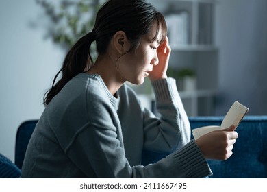 A depressed woman sitting on a sofa and holding a passbook