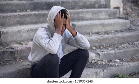 Depressed young black male sitting outside, emotional abuse, family problem