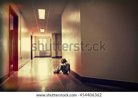 Depressed young boy sitting alone in a hallway