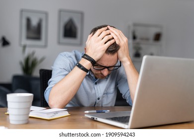 Depressed young businessman holding head in hands, has problem, a laptop on the desk. A guy made a mistake in a work