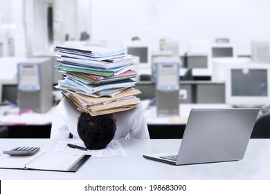 Depressed young businessman with a pile of documents on his head at office