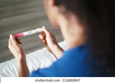 Depressed young hispanic woman with anxious feelings on bed. Black girl holding negative pregnancy test. Close-up of hands and kit
