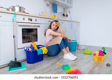 Depressed Young Housewife Feeling Tired From Domestic Chores, Sitting On Floor At Kitchen. Young Lady With Cleaning Supplies Exhausted From House Cleaning, Suffering From OCD Disorder