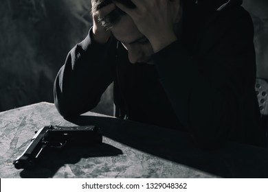 Depressed young man with gun at table. Suicide awareness concept