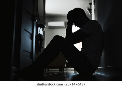 Depressed young man sitting on floor in dark room. Silhouette of young male suffering from loneliness and anxiety, covering his face with hands. Person with mental disorder - Powered by Shutterstock - Get 15% off with code: PIKWIZARD15