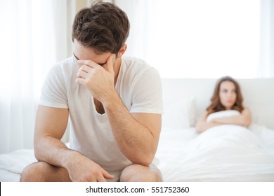 Depressed young man sitting on bed and having problems with his girlfriend