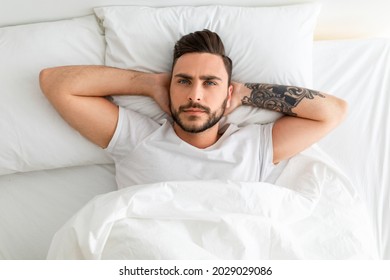 Depressed Young Man Unable To Sleep, Lying In Bed, Looking Up And Contemplating, Top View. Sleeplessness, Mental Health Problem, Male Depression Concept