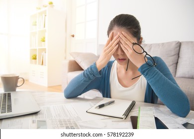 depressed young mixed race asian woman use hands cover her face after checking bills and bank account balance sitting on sofa in the living room at home. interior and domestic housework concept.