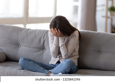 Depressed young woman covering face by hands, crying alone at home, upset girl sitting on sofa, feeling unhappy after quarrel or breakup, despair and lonely, psychological problem concept - Shutterstock ID 1325841596