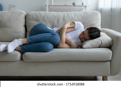 Depressed young woman lying on couch on living room feeling distressed lonely after breakup or divorce, upset unhappy millennial female mourn yearn on sofa, suffer after miscarriage or abortion