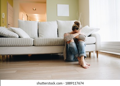 Depressed young woman sitting on floor at home.