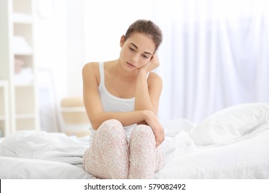 Depressed Young Woman Sitting On Bed At Home