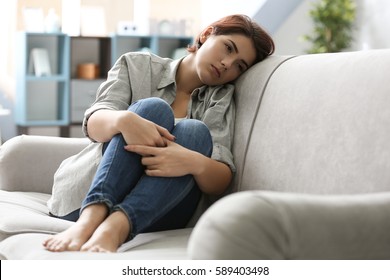 Depressed young woman sitting on sofa at home