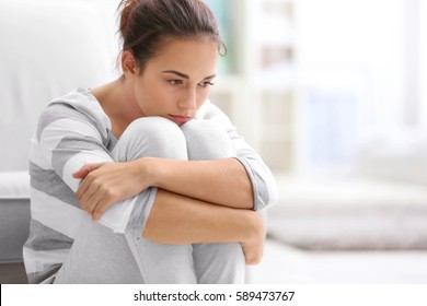 Depressed young woman sitting on floor at home