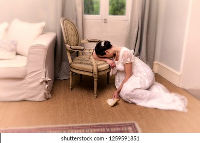Depressend youg woman in authentic regency dress holding a letter and leaning against an antique chair