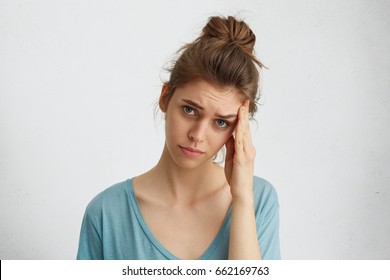 Depressing Doleful Woman With Hair Knot, Blue Exhausted Eyes Touching Her Head Having Discontented Expression Being Tired After Work. Dull Female Having Headache After Sleepless Night. Feeling Concept