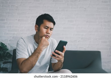 Depression Concept. Asian Man Sad And Checking Mobile Phone Sitting On The Sofa In The Living Room At Home, Asian Man Serious And Worry While Using Mobile Phone.