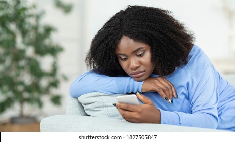 Depression Concept. Portrait Of Frustrated African American Woman Looking At Smartphone, Checking Social Media, Lying On The Couch. Upset Black Lady Waiting For His Message Or Call, Reading Bad News