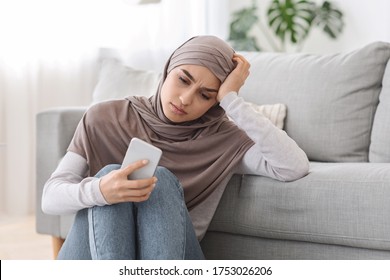 Depression Concept. Upset Arabic Woman In Hijab Sitting With Smartphone On Floor At Home, Received Bad News, Feeling Lonely