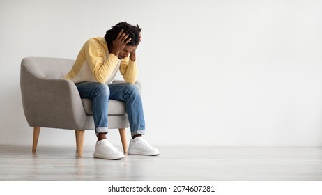 Depression Concept. Upset young black man sitting in armchair and touching head in despair, millennial african american guy suffering problems, feeling depressed and lonely, panorama with copy space - Shutterstock ID 2074607281