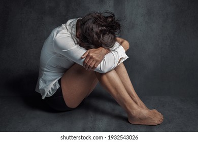 Depression or domestic violence concept: Sad lonely young woman crying while sitting on the floor in a dark room with an attitude of sadness and boredom with her legs together and hugged.