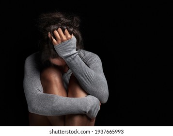 Konzept der Depression oder häuslichen Gewalt: Traurige einsame junge Frau weinend, während sie im dunklen Raum saß, mit einer Einstellung der Traurigkeit und Langeweile mit ihren Beinen zusammen und umarmt.