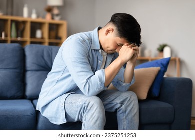 Depression Issue. Upset Korean guy crying resting head on fists, revealing sadness through his expression sitting at home, Moment of vulnerability and solitude, emotional distress concept - Powered by Shutterstock