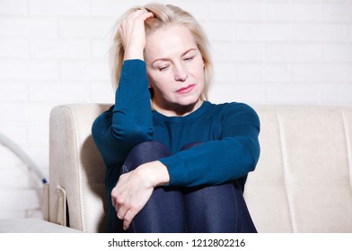 Depression. Middle Aged Woman Barefoot Sitting On The Couch, Hugging Her Head, At Home. The Concept Of Sadness And Loneliness.