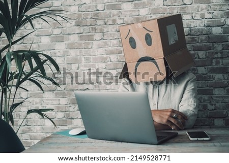 Depression and problems working alone at home in smart work modern job. Woman with sad carton box covering head looking her laptop computer. Password and privacy security online concept. Crypto market