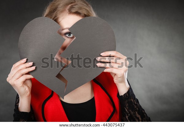 Depression and sadness concept. Young
person with broken heart full of negative sad emotions. Woman
covering his face by two parts of black love
symbol.